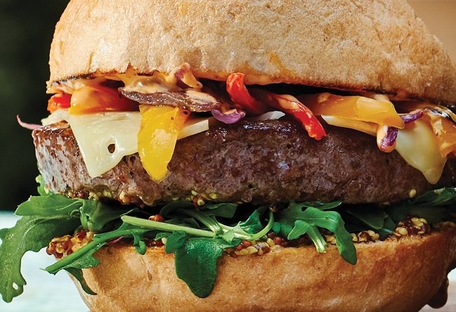 Hamburger with beef patty, cheese, vegetables, and arugula on a bun.