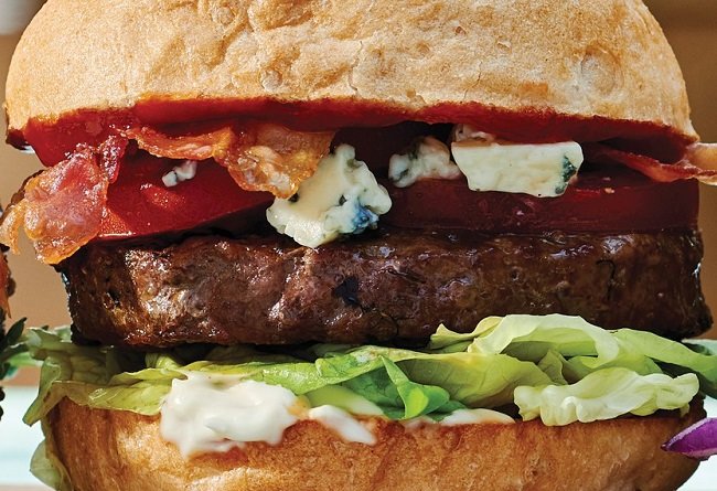 Close-up of a beef burger with bacon, blue cheese, and lettuce on a bun.