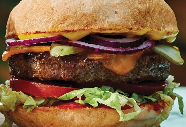 Close-up of a juicy burger with various ingredients on a bun.