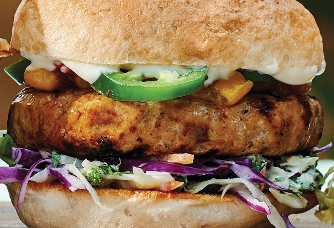 Close-up of a cooked from frozen Gourmet Chicken Burger with various toppings on a bun.