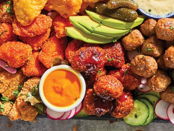 Platter of cooked from frozen appetizers with pickles, avocado, and a dipping sauce.