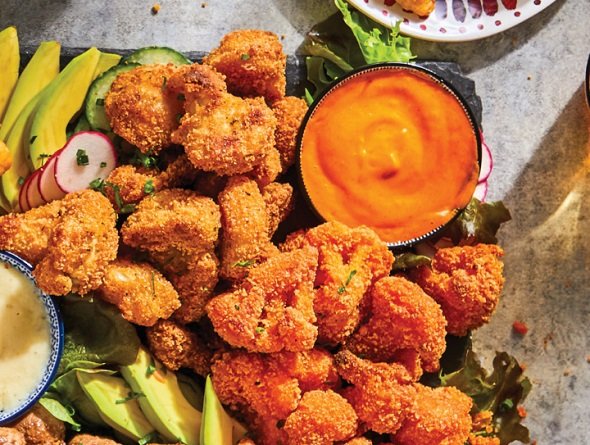 Breaded cauliflower with dipping sauces and vegetables on a platter