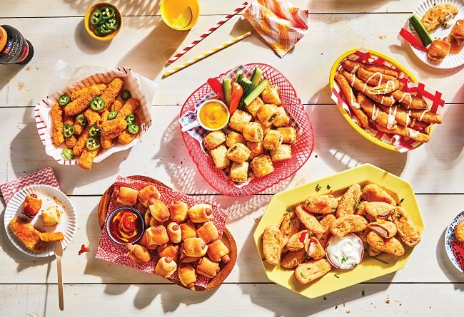 Assorted made-from-frozen foods on a white wooden table with condiments and straws.