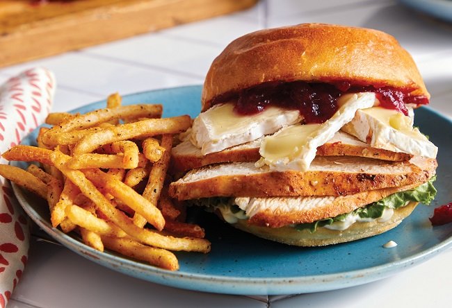 Sandwich with turkey, cheese, and cranberry sauce on a blue plate with fries.