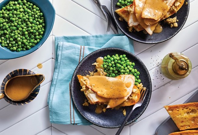 Two plates of turkey, gravy and green on a white table.