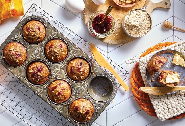 Muffin tin with baked muffins on a kitchen counter with ingredients and a plate of muffins.