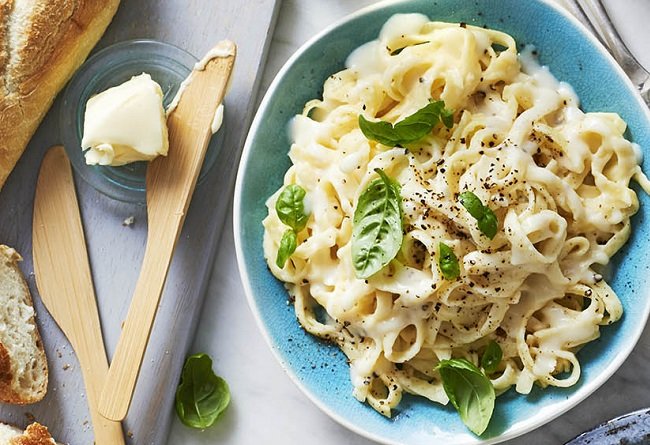 Pasta dish with greens in a blue bowl on a table with bread and butter.