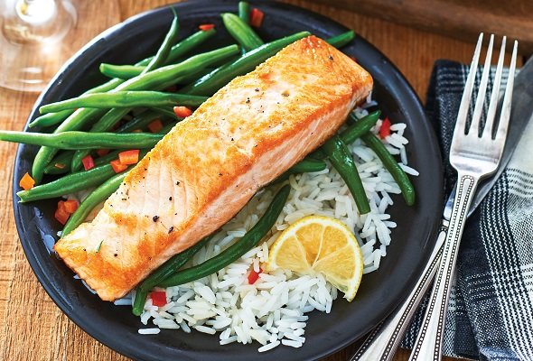 Salmon fillet with green beans and rice on a black plate with silverware.