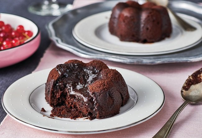 Chocolate lava cake on a white plate with a pink tablecloth and red berries in the background.