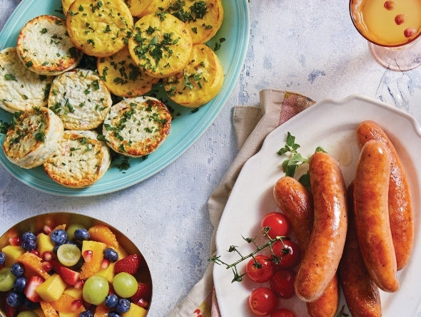 Assorted brunch foods including sausages, fruit salad, and omelette bites on a table.