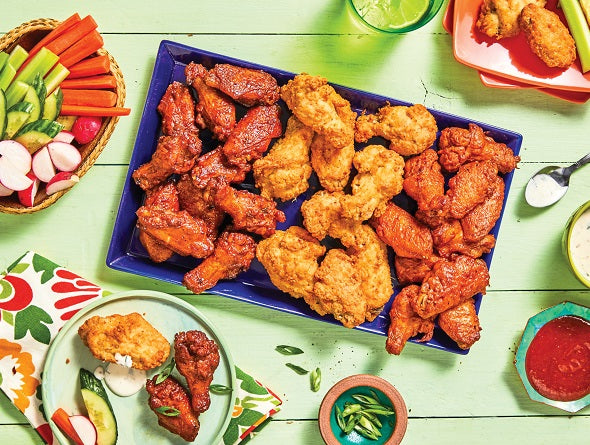 Assorted fried chicken wings on a blue platter with side dishes on a green wooden table.