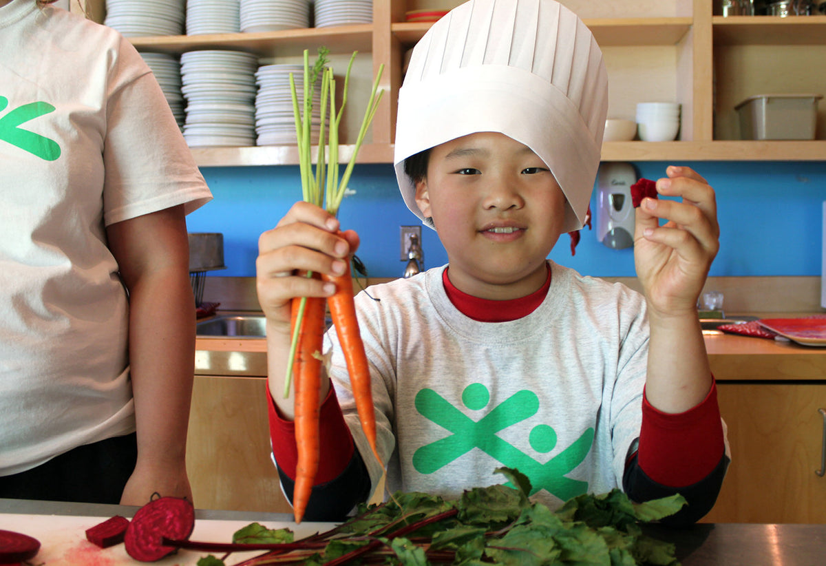 Child holding carrots and radishes in a kitchen setting