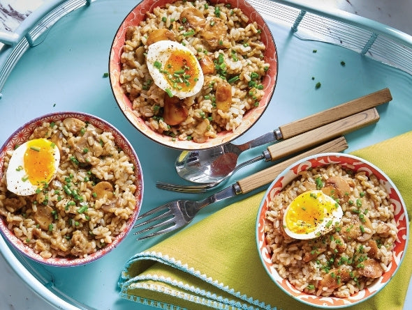 Three bowls of Mushroom Risotto with eggs and vegetables on a blue tray with cutlery.