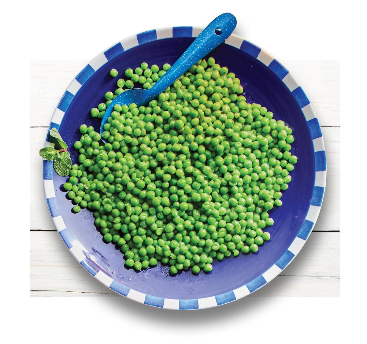 Blue plate with cooked frozen green peas and a blue spoon on a white wooden surface