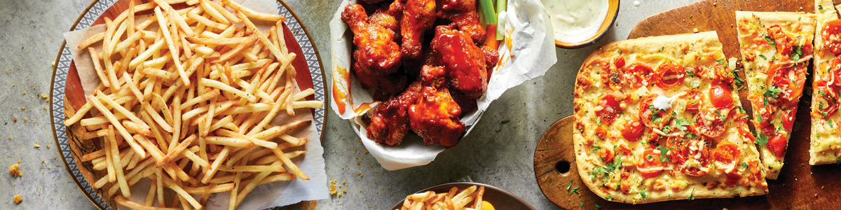 A spread of game-time ready foods made from frozen, including french fries, wings and flatbread.