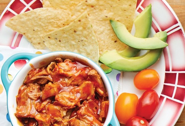 Bowl of Pulled Pork with tortilla chips, avocado, and cherry tomatoes on a colorful plate.